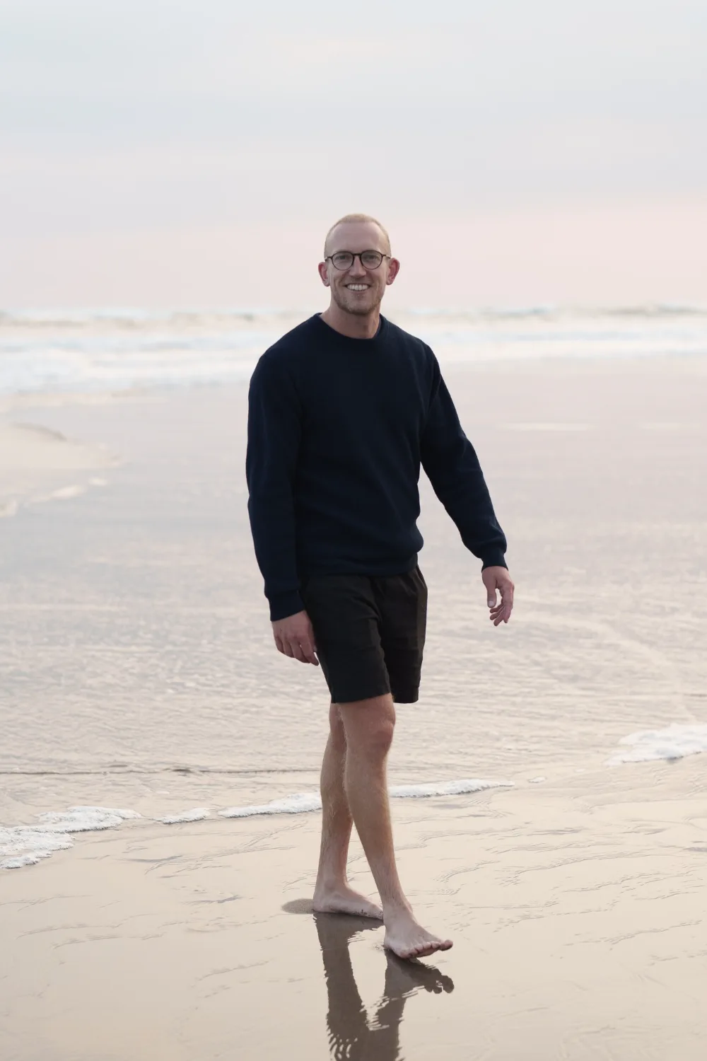 Lawrence standing barefoot at the water’s edge on an Australian beach