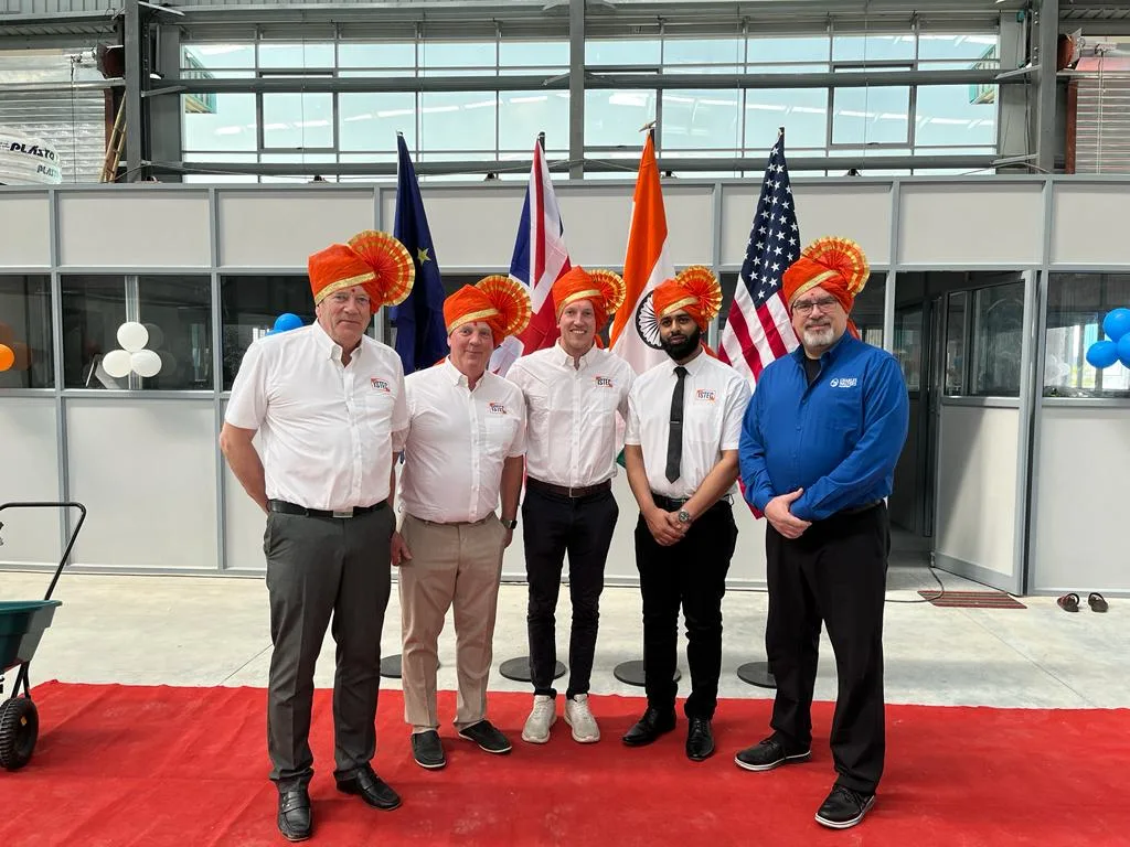 Five members of the international team wearing ceremonial turbans inside the ISTEC factory, in front of EU, UK, Indian and US flags